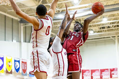 A male basketball player goes for a layup while guarded by two opponents.